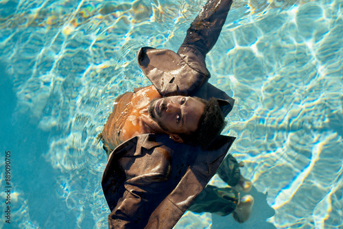 Man in a suit floating serenely on his back in a clear blue swimming pool under the sunlight.