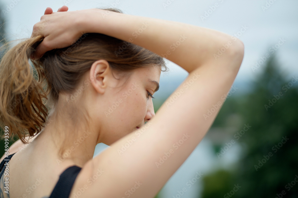Close-up of a young woman tying her hair in a natural outdoor setting. Close-up of a young woman tying her hair in a natural outdoor setting.