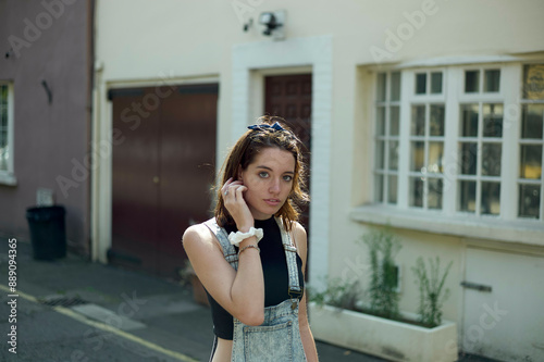 Young woman standing by a white doorway in an alley, with a thoughtful expression as she touches her hair. photo