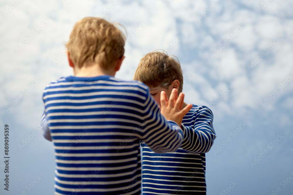Two young children in striped shirts stand against a backdrop of clouds, with one comforting the other by placing a hand on their shoulder. Two young children in striped shirts stand against a backdrop of clouds, with one comforting the other by placing a hand on their shoulder.