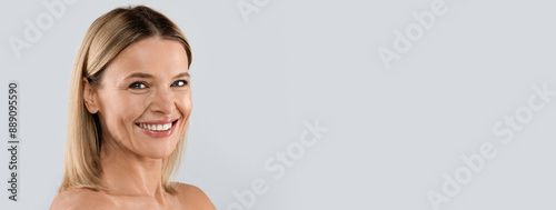 Youthful appearance, aesthetic medicine, injection cosmetology concept. Closeup studio shot of pretty cheerful middle aged blonde woman posing on grey background, smiling at camera, copy space photo