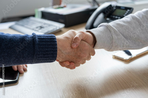 Two individuals engage in a firm handshake over a wooden desk in an office setting photo