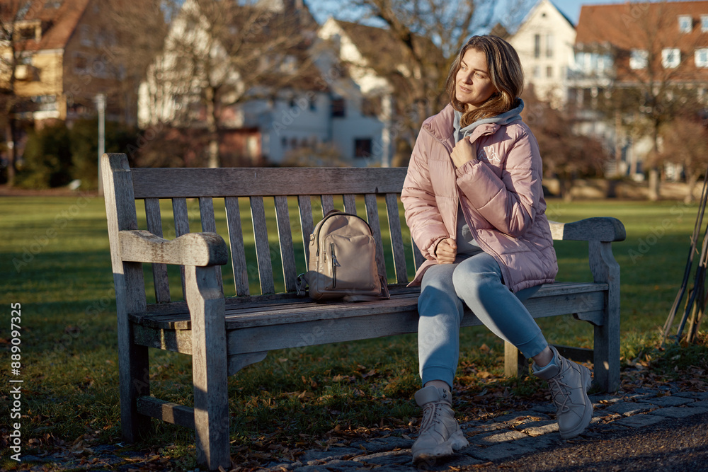 Obraz premium Beautiful Girl in Pink Jacket Enjoys Festive Atmosphere in Bitigheim-Bissingen Park. girl in a pink winter jacket sits bench in a park historic town of Bitigheim-Bissingen, Baden-Württemberg, Germany.