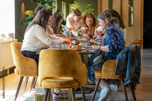 A group of women enjoy a meal together at a stylishly furnished restaurant with golden velvet chairs and warm lighting. photo