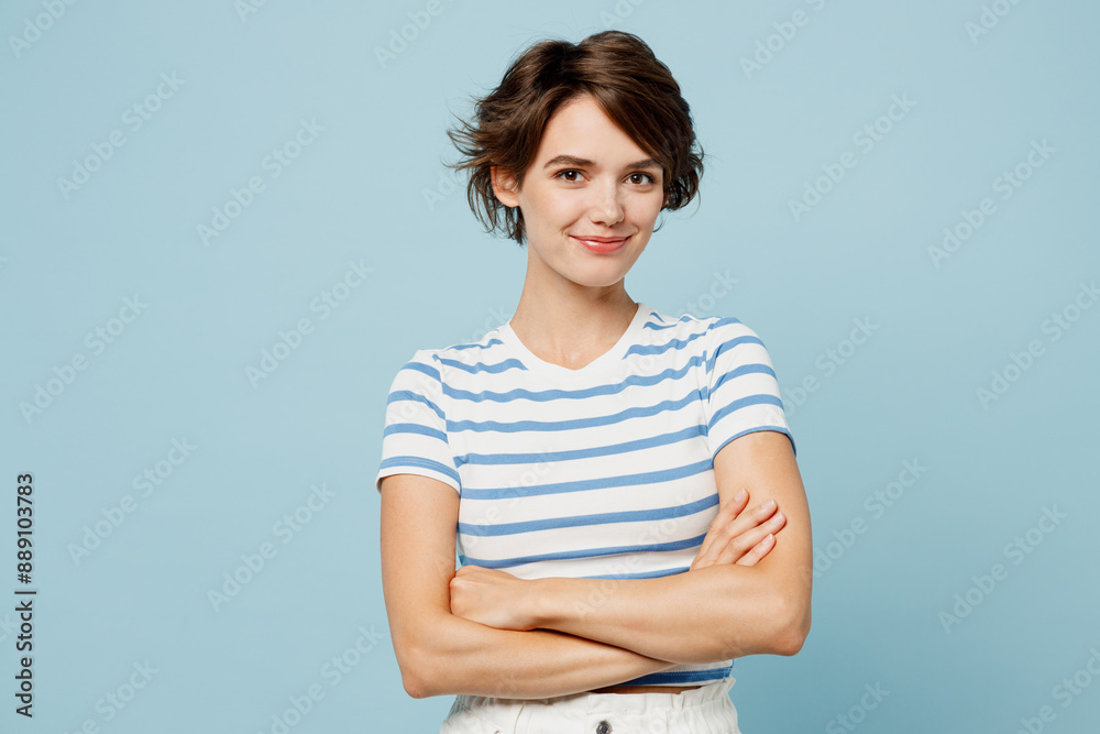© ViDi Studio - Young smiling cheerful woman wearing striped t-shirt casual clothes hold hands crossed folded look camera isolated on plain pastel light blue cyan color background studio portrait. Lifestyle concept.