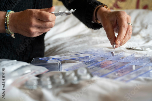 Adult hands organizing medications into a pill organizer on a table with various blister packs and pill bottles.