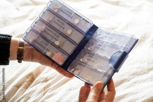 Hand holding a pill organizer with compartments labeled with days of the week in different languages, filled with various pills. photo