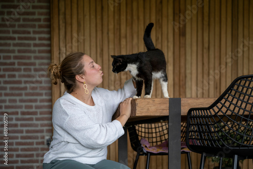 Woman interacts affectionately with a black and white cat perched on a wooden table.