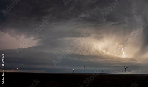 A dramatic nighttime scene of a lightning bolt striking amidst wind turbines under a tumultuous stormy sky.