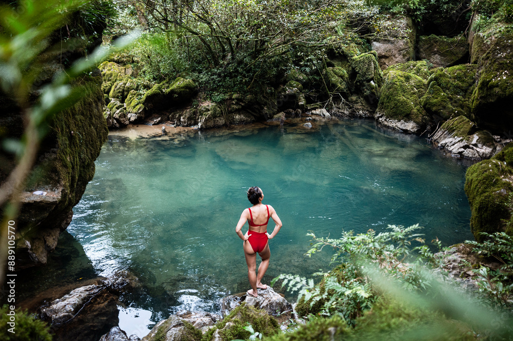 Woman in a red swimsuit standing by a serene forest pond. Woman in a red swimsuit standing by a serene forest pond.