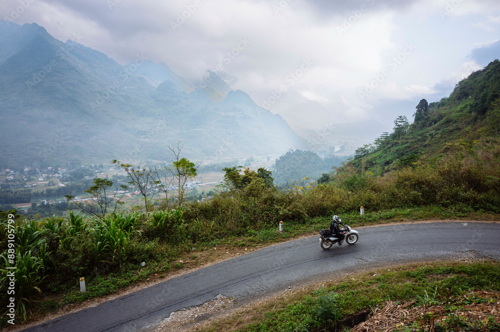 Motorcyclist riding on a curving mountain road with misty hills in the background. Motorcyclist riding on a curving mountain road with misty hills in the background.