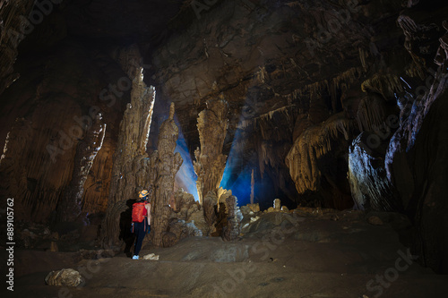 A person explores a vast cave with impressive stalactites and stalagmites illuminated by natural light. photo