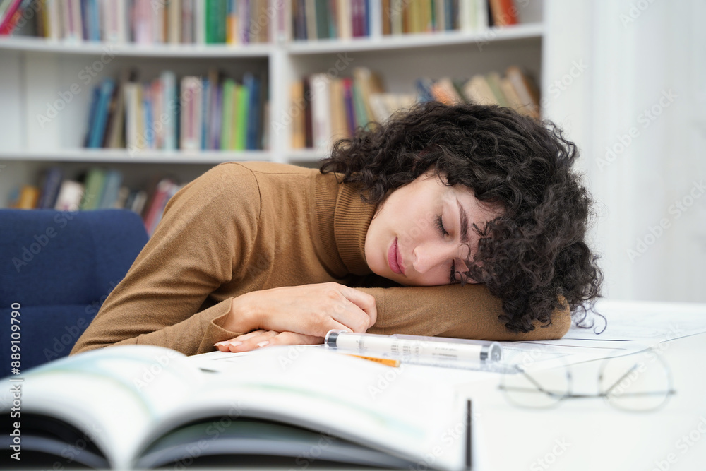 Tired female architect working in library with blueprints and falling asleep Tired female architect working in library with blueprints and falling asleep