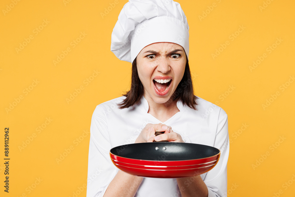Young shocked sad surprised chef cook baker woman wear white shirt black apron uniform toque chefs hat hold frying pan with burnt meal isolated on plain yellow background studio Cooking food concept.