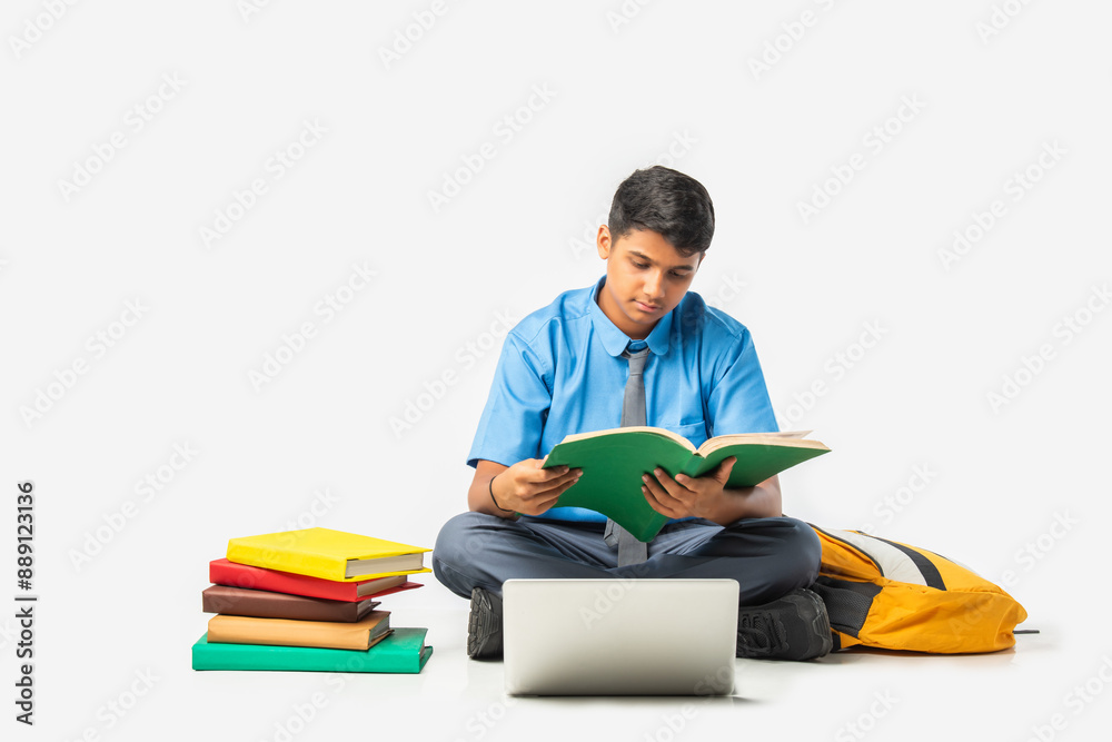 Asian Indian schoolboy with books and laptop, pointing at blank space, promoting education Asian Indian schoolboy with books and laptop, pointing at blank space, promoting education