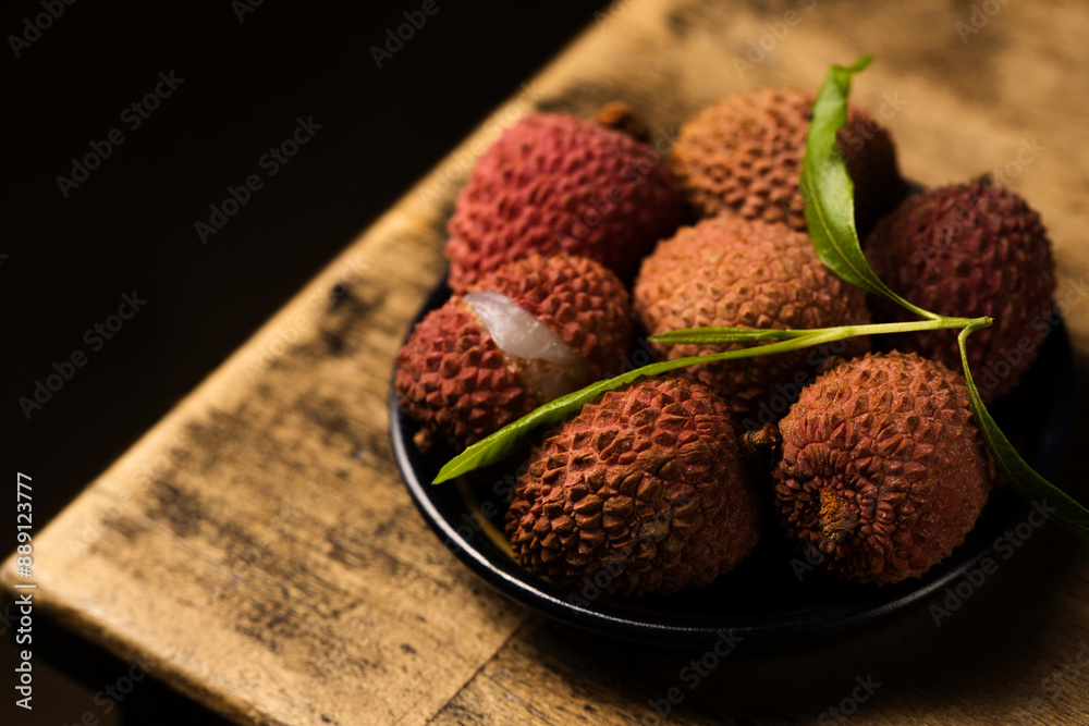 Tropical lychee berries on a black plate on a wooden background Tropical lychee berries on a black plate on a wooden background