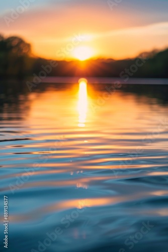 The sunset reflecting off the surface of a calm river, with a softly blurred background of surrounding trees and sky. 