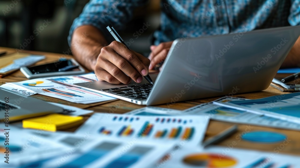 Financial analyst preparing a detailed financial report using a laptop and multiple reference documents The workspace is tidy and professional, with graphs and charts prominently displayed Financial analyst preparing a detailed financial report using a laptop and multiple reference documents The workspace is tidy and professional, with graphs and charts prominently displayed