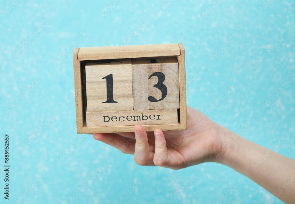 woman's hand holds wooden block calendar with the date December 13 on blue concrete background woman's hand holds wooden block calendar with the date December 13 on blue concrete background