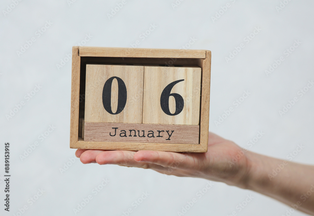 Woman's hand holds wooden block calendar with the date January 06 on white concrete background Woman's hand holds wooden block calendar with the date January 06 on white concrete background