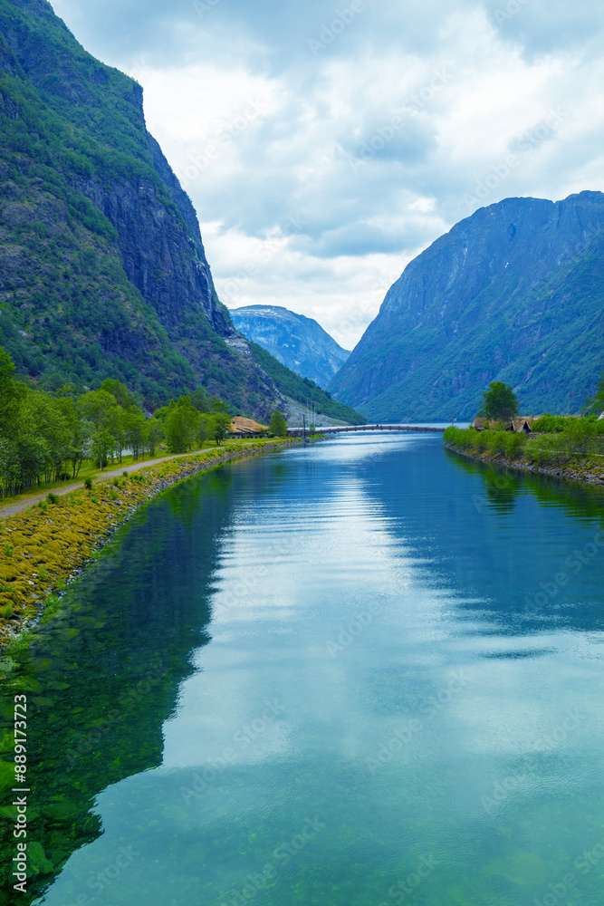 The mouth of the Naeroydalselvi river in the village of Gudvangen on Naeroyfjord on a cloudy day. Reflection of mountains in water. Beautiful nature of Norway. Vertical image