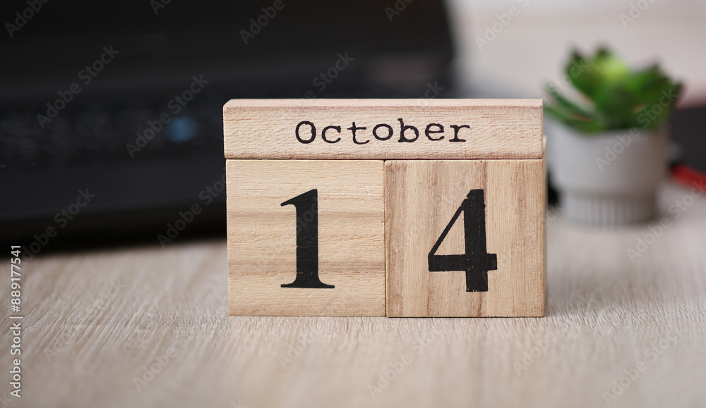 Wooden calendar with the date October 14 on desktop with laptop Wooden calendar with the date October 14 on desktop with laptop