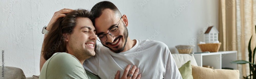 Fototapeta premium Two men embrace on a couch, smiling and laughing together.