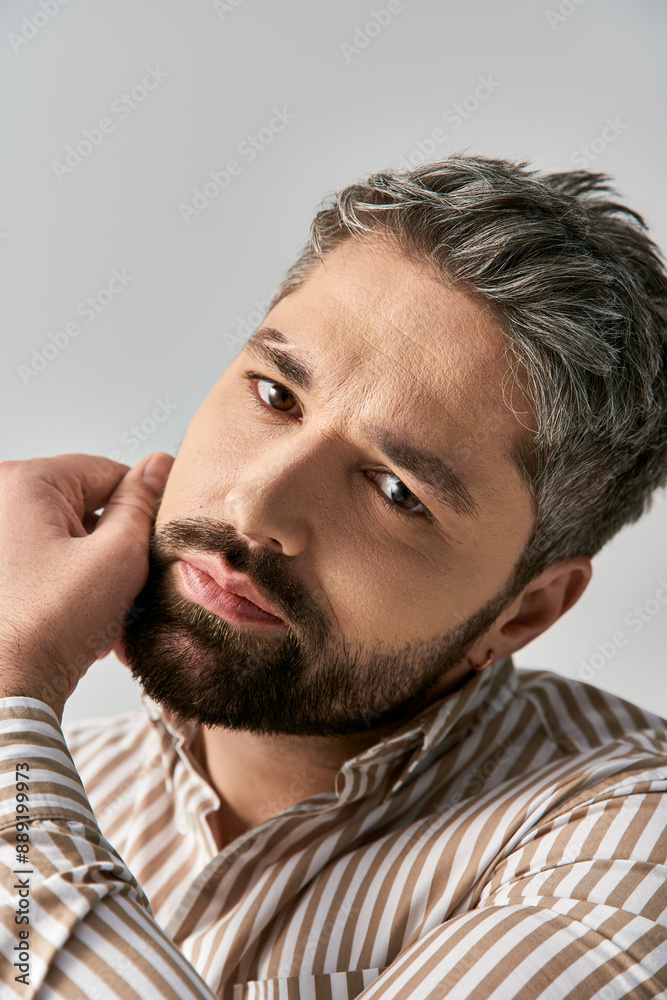 Obraz premium A stylish man with a beard exuding charm in a striped shirt against a neutral studio backdrop.