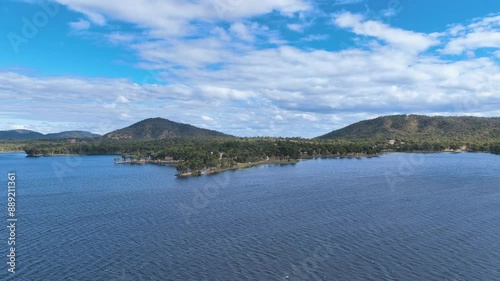 Flight across the small waves of Lake Eungella, Sunwater's water reservoir for the MacKay region of Queensland Australia. Approaches multiple headlands and camping ground site with forested hills. photo