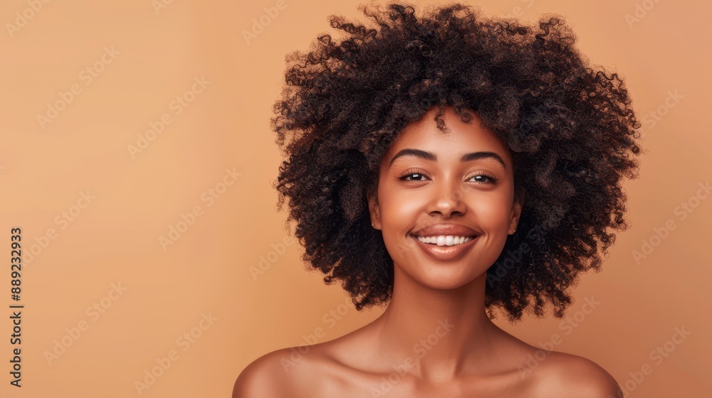 Smiling African American woman with natural curly hair and bare shoulders against a warm beige background, radiating confidence and beauty.