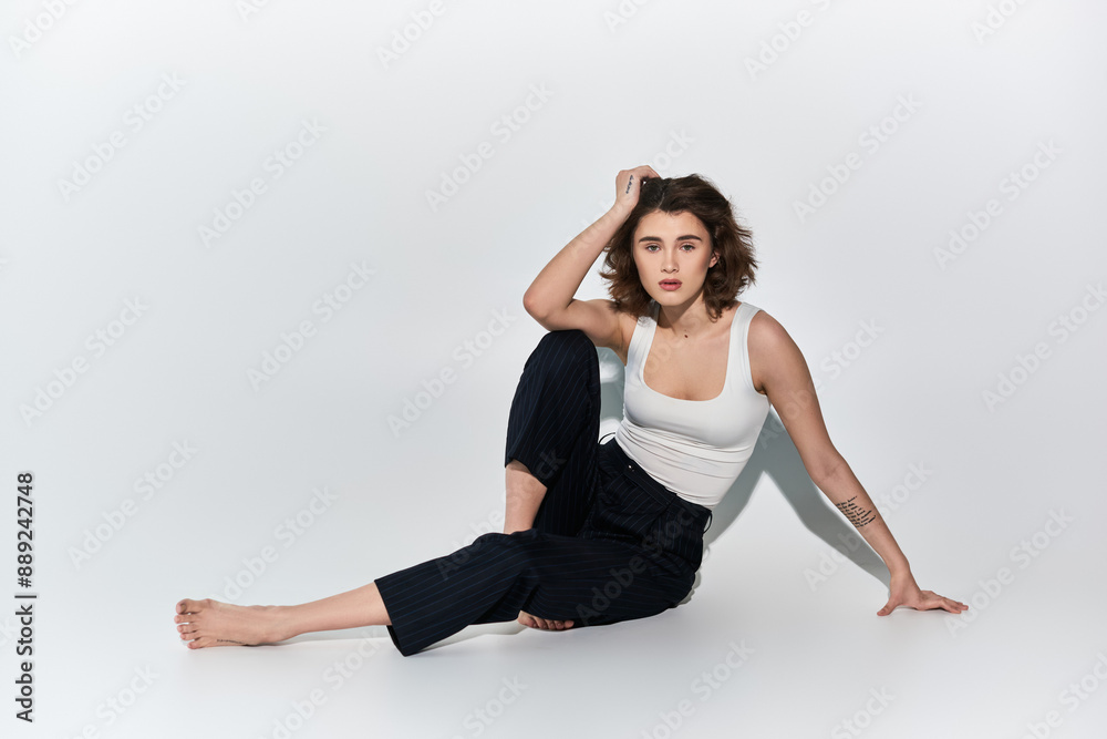 A pretty young woman sitting gracefully on the ground with her legs crossed, dressed in black pants and a white tank top. A pretty young woman sitting gracefully on the ground with her legs crossed, dressed in black pants and a white tank top.