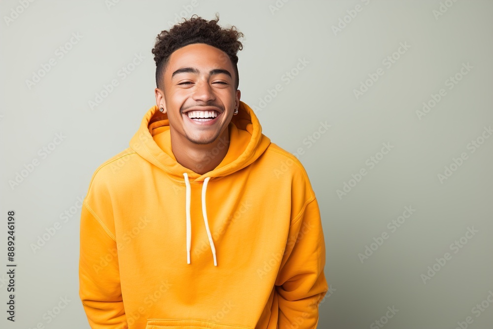 A young man wearing a yellow hoodie is smiling and looking at the camera A young man wearing a yellow hoodie is smiling and looking at the camera