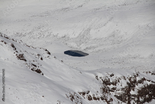 Shot of blue crater lake in snowy mountains. Clear water, snow-capped peaks. Lake surrounded by snow-covered mountains, deep blue sky. Perfect place to relax in nature. photo