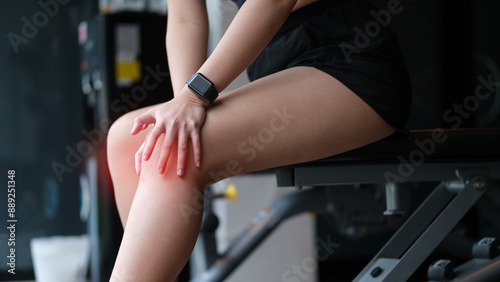 Close up image of female athlete feeling pain and holding her injured knee during exercise at the gym.
