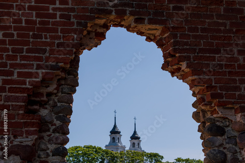 view of a white church through the broken windows of a red brick medieval castle
