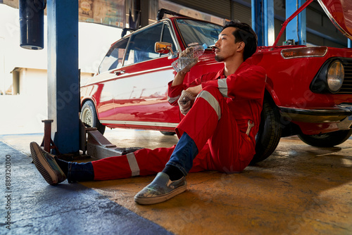 Asian technician male take a brake for drink a water after finish from repair a red retro car in garage.