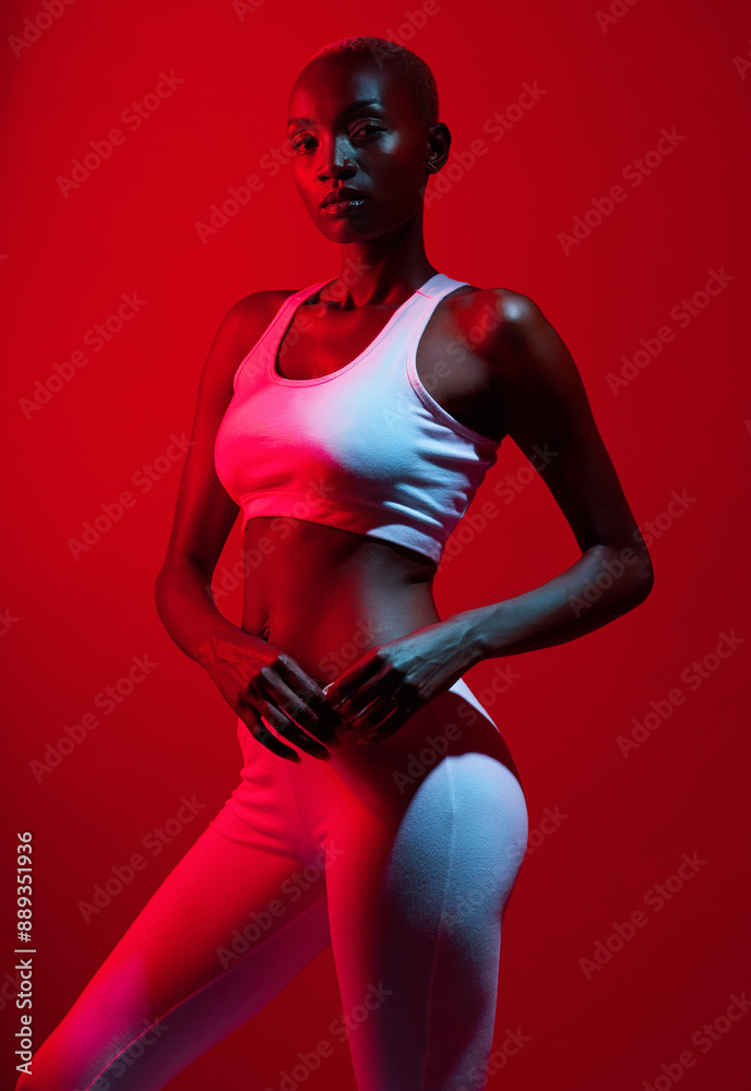 Fototapeta premium Red light, black woman and sportswear in studio with confidence for fitness, workout and exercise. Female person, portrait and serious on bodybuilding with training for body health and wellness