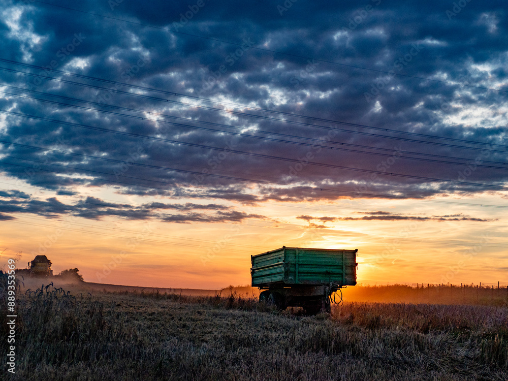 Fototapeta premium Mähdrescher bei der Ernte zu Sonnenuntergang