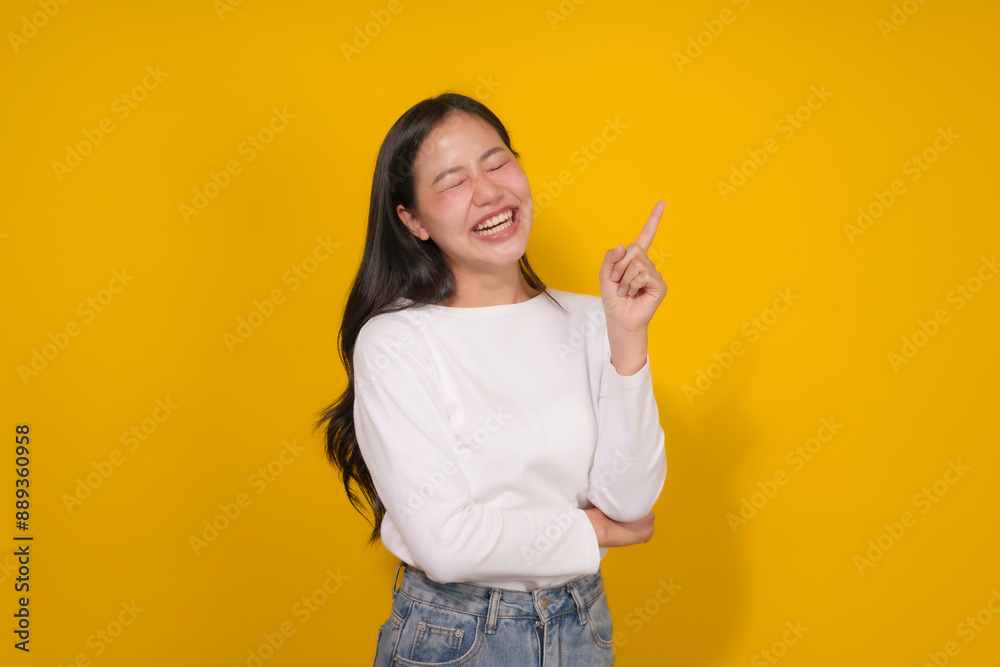 Young woman is pointing and smiling with her eyes closed on a yellow background, suggesting a positive and engaging concept Young woman is pointing and smiling with her eyes closed on a yellow background, suggesting a positive and engaging concept