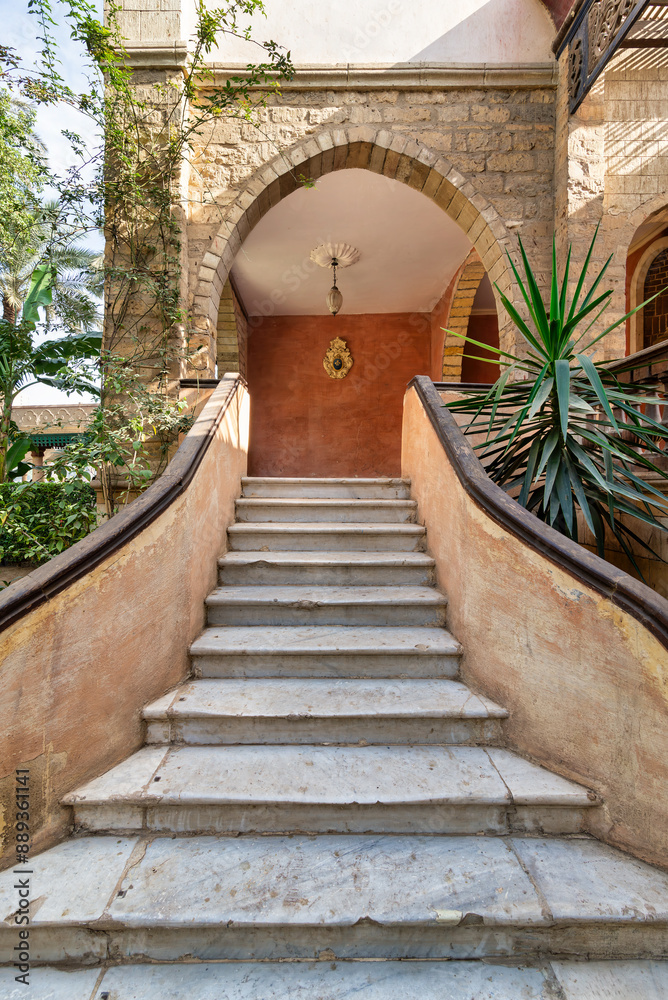 White marble staircase with stone railings, flanked by sculptures, that descends to a serene courtyard surrounded by lush greenery and tropical plants White marble staircase with stone railings, flanked by sculptures, that descends to a serene courtyard surrounded by lush greenery and tropical plants