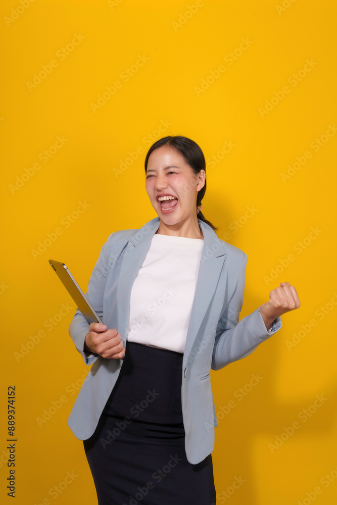 Young businesswoman is celebrating a success in a studio, holding a tablet in one hand and raising her fist in the air