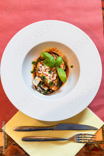 aubergine parmigiana with basil leaf in a deep white dish, classic Italian preparation photo