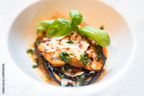 aubergine parmigiana with basil leaf in a deep white dish, classic Italian preparation