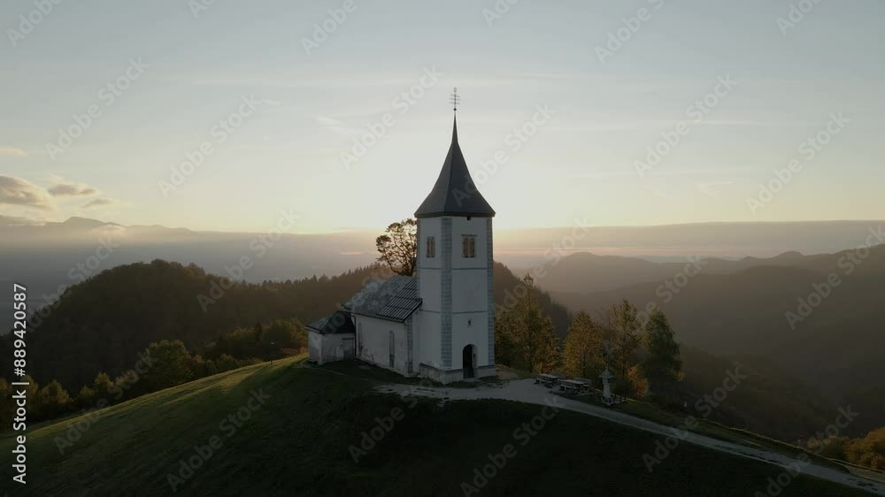 Aerial view of St. Primoz church at sunrise on a hill with mountain peaks in Julian Alps, Jamnik, Slovenia. Aerial view of St. Primoz church at sunrise on a hill with mountain peaks in Julian Alps, Jamnik, Slovenia.