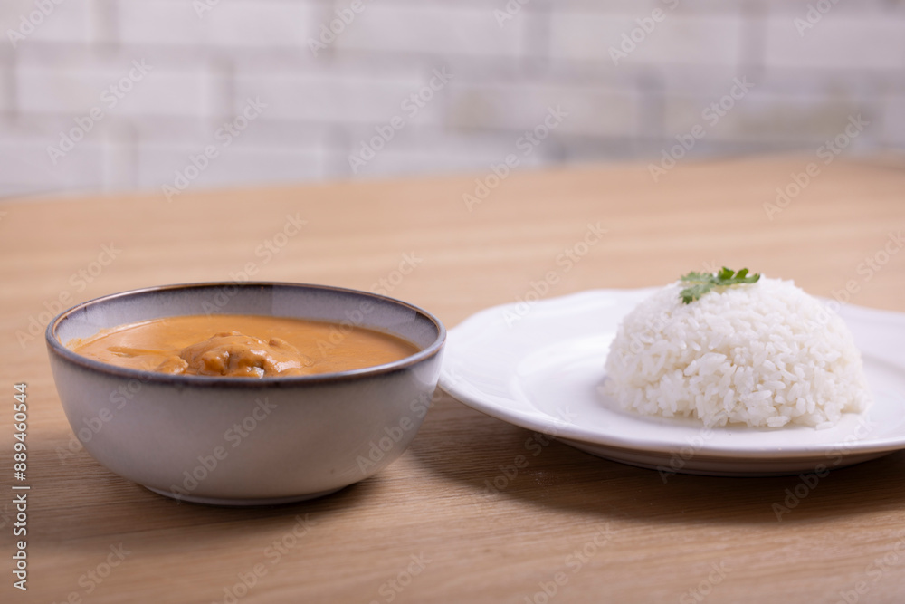 Delicious bowl of creamy butter chicken served with a mound of steamed white rice garnished with cilantro on a white plate, accompanied by a refreshing orange juice in a plastic cup. Delicious bowl of creamy butter chicken served with a mound of steamed white rice garnished with cilantro on a white plate, accompanied by a refreshing orange juice in a plastic cup.