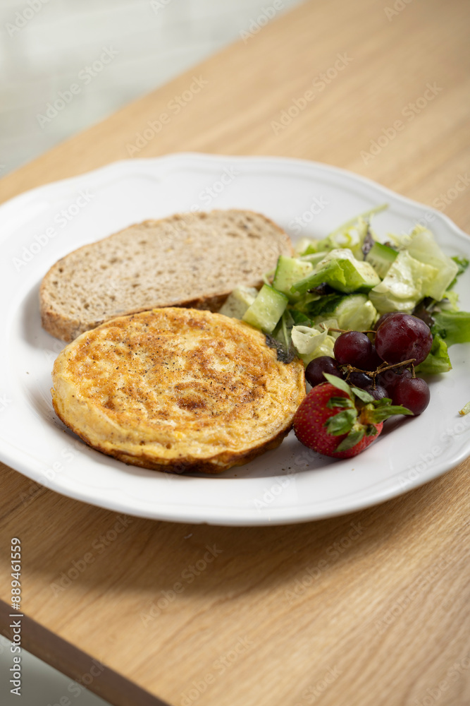 A delicious breakfast plate featuring a golden-brown omelette, two slices of whole grain bread, a fresh mixed green salad, red grapes, and a ripe strawberry. A nutritious and balanced meal ideal. A delicious breakfast plate featuring a golden-brown omelette, two slices of whole grain bread, a fresh mixed green salad, red grapes, and a ripe strawberry. A nutritious and balanced meal ideal.