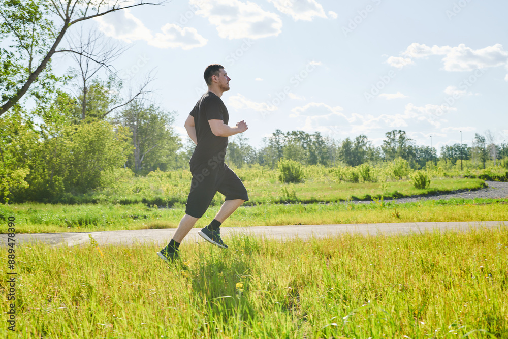 A male athlete is training on the sports ground outside. Caucasian male athlete jogging outdoors in a summer park A male athlete is training on the sports ground outside. Caucasian male athlete jogging outdoors in a summer park