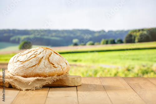 Loaf of traditional bread on a kitchen cloth on wooden table on a background of green wheat field. Copy space for products.