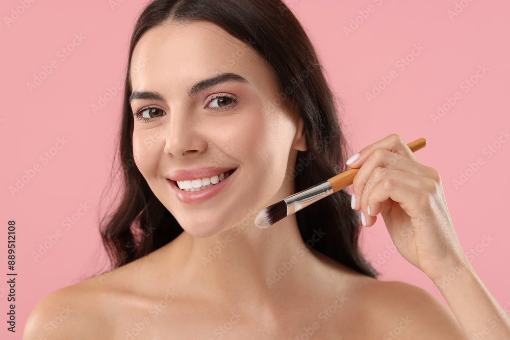 Smiling woman applying makeup with brush on pink background Smiling woman applying makeup with brush on pink background