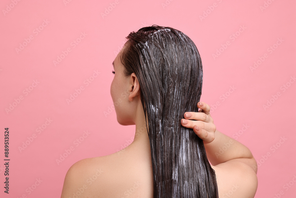 Woman applying hair mask on pink background, back view Woman applying hair mask on pink background, back view
